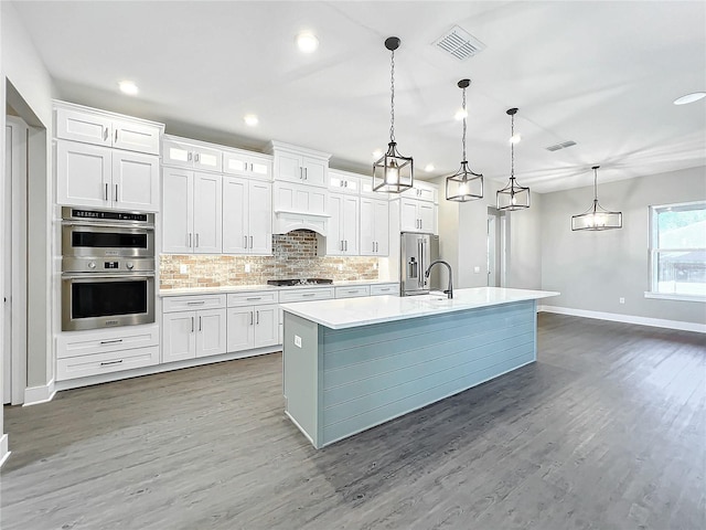 kitchen featuring appliances with stainless steel finishes, decorative light fixtures, white cabinetry, and an island with sink