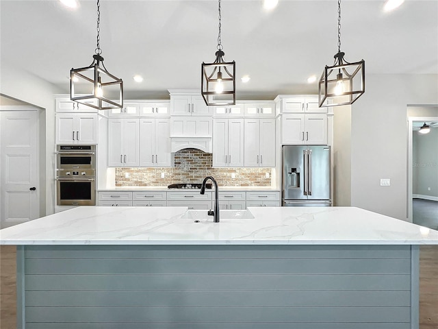 kitchen with appliances with stainless steel finishes, light stone counters, pendant lighting, and sink