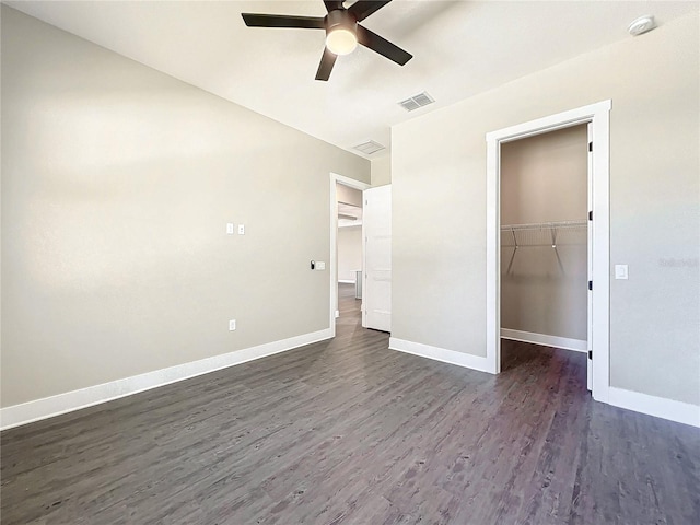 unfurnished bedroom featuring a walk in closet, ceiling fan, a closet, and dark wood-type flooring