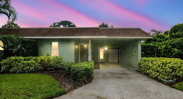 exterior space featuring a shingled roof, an attached carport, concrete block siding, and driveway