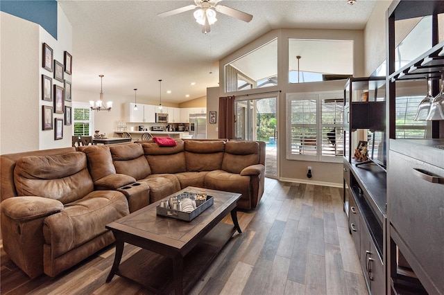 living room featuring a textured ceiling, ceiling fan with notable chandelier, dark wood-type flooring, and vaulted ceiling