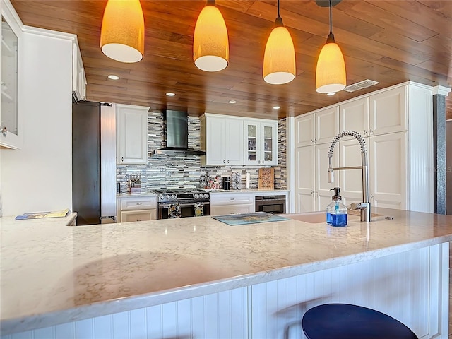 kitchen with stainless steel range oven, wall chimney exhaust hood, light stone countertops, white cabinets, and decorative light fixtures
