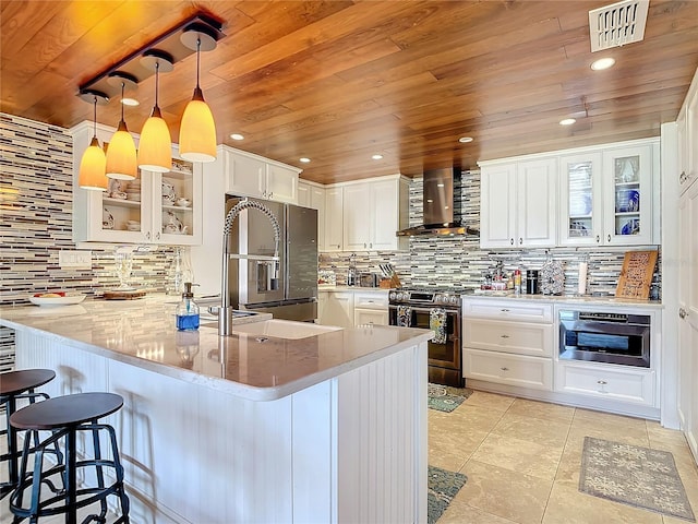 kitchen with appliances with stainless steel finishes, wall chimney exhaust hood, kitchen peninsula, white cabinets, and light stone countertops