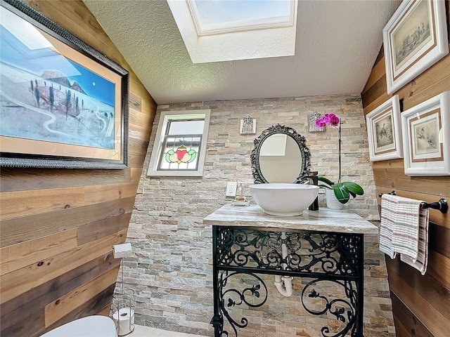 bathroom with vanity, a textured ceiling, a skylight, and wooden walls