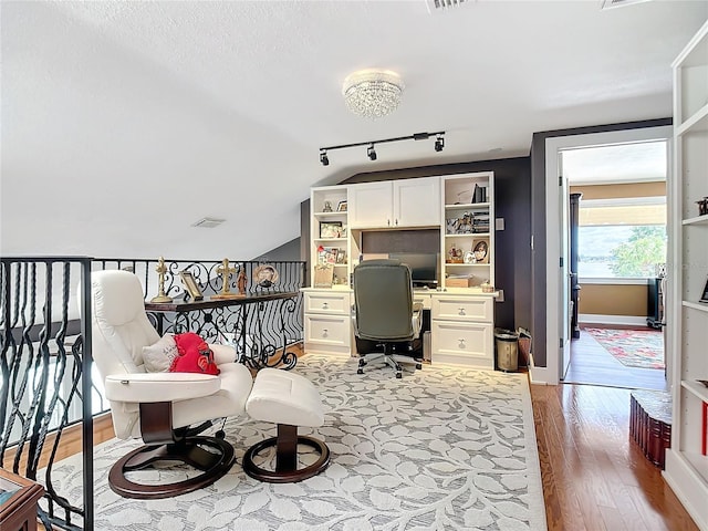 home office featuring rail lighting, light hardwood / wood-style floors, and vaulted ceiling