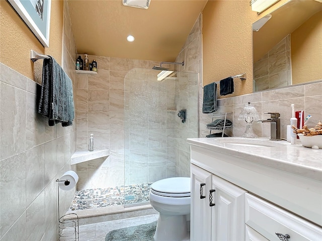 bathroom featuring tile walls, vanity, a tile shower, and toilet