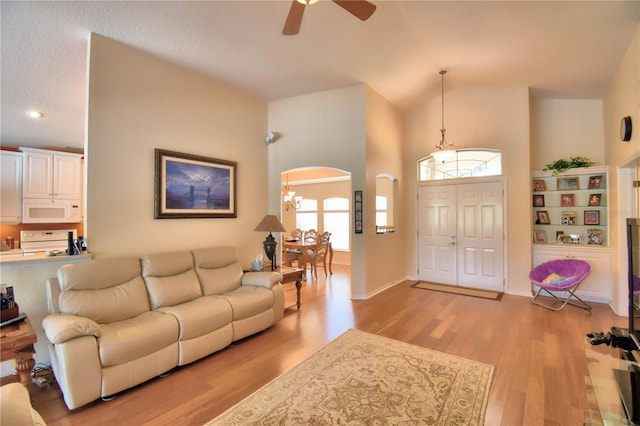 living room with light wood-type flooring, high vaulted ceiling, and ceiling fan with notable chandelier