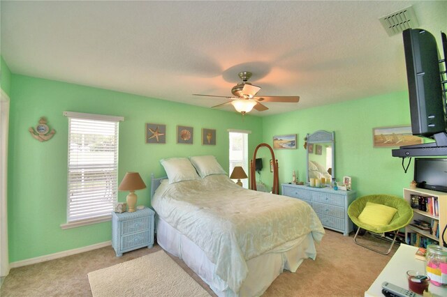 bedroom with ceiling fan, a textured ceiling, light carpet, and multiple windows