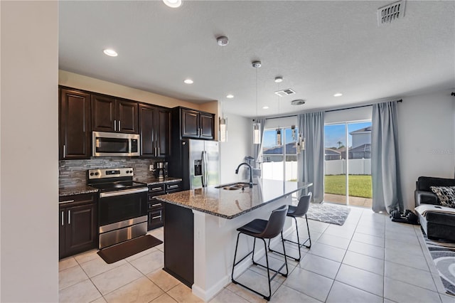 kitchen featuring decorative light fixtures, stainless steel appliances, an island with sink, a breakfast bar area, and backsplash