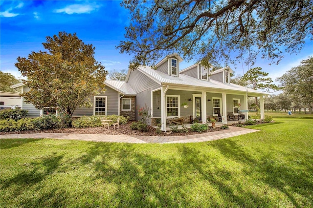 cape cod home with metal roof, stone siding, covered porch, and a front yard