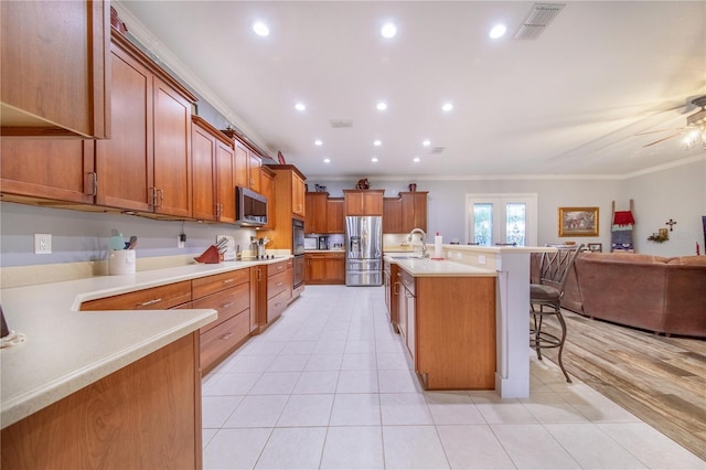 kitchen with ceiling fan, light wood-type flooring, ornamental molding, a breakfast bar area, and appliances with stainless steel finishes