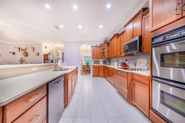 kitchen featuring arched walkways, glass insert cabinets, stainless steel appliances, light countertops, and a sink