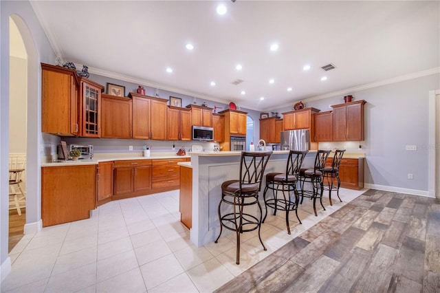 kitchen featuring crown molding, a kitchen bar, light hardwood / wood-style floors, appliances with stainless steel finishes, and a center island with sink