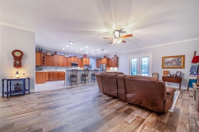 living room with ornamental molding, french doors, ceiling fan, and light wood-type flooring