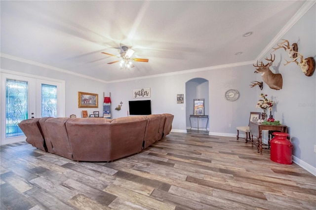 living area with arched walkways, ceiling fan, wood finished floors, baseboards, and crown molding