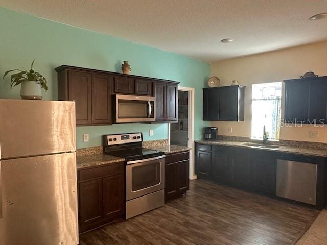 kitchen with stainless steel appliances, a sink, dark brown cabinets, and dark wood-style floors