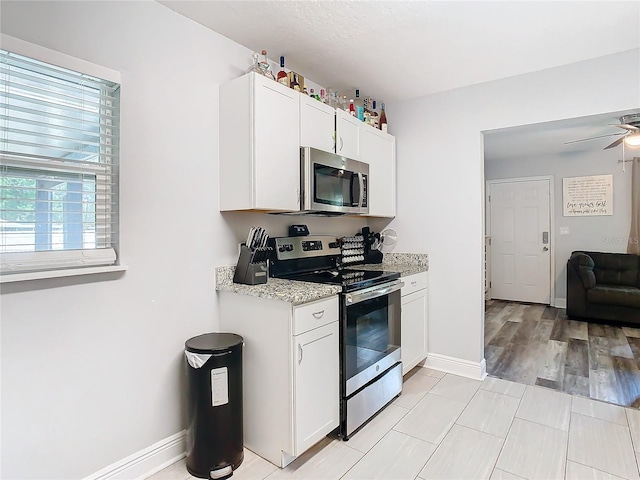 kitchen featuring stainless steel appliances, white cabinetry, ceiling fan, and light stone counters