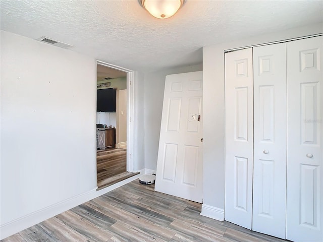 unfurnished bedroom featuring a textured ceiling, light wood-type flooring, and a closet