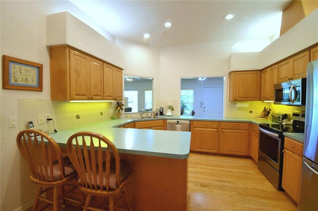 kitchen featuring kitchen peninsula, sink, light wood-type flooring, stainless steel appliances, and a breakfast bar area