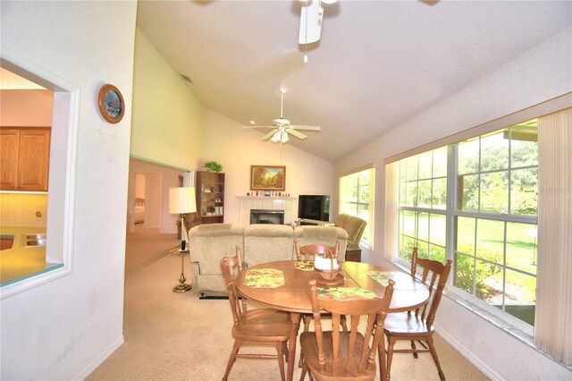 dining space with a fireplace, light carpet, plenty of natural light, ceiling fan, and vaulted ceiling