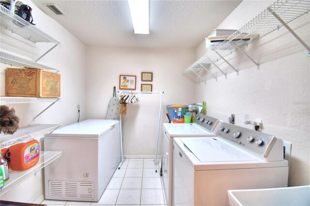 laundry area featuring sink, light tile patterned flooring, a textured ceiling, and independent washer and dryer