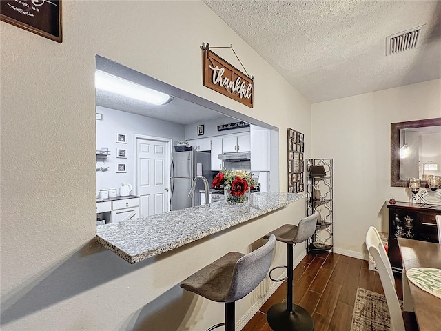 kitchen with a kitchen breakfast bar, kitchen peninsula, a textured ceiling, and stainless steel refrigerator