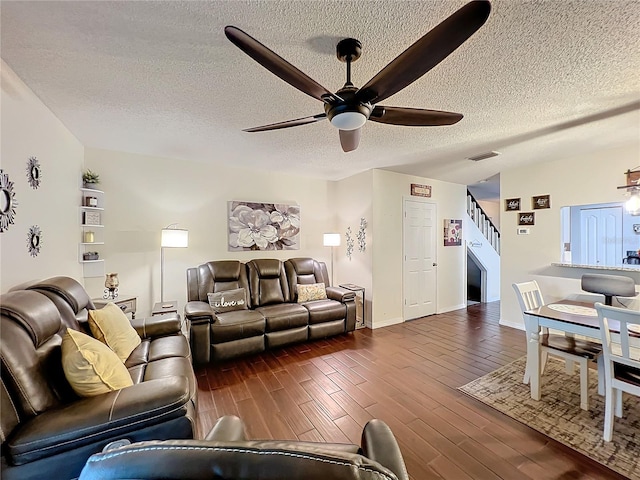 living room with a textured ceiling, ceiling fan, and dark wood-type flooring