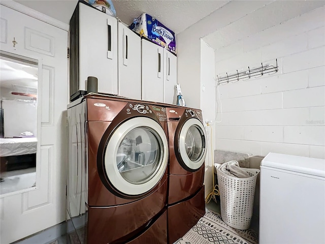 laundry area with cabinets, a textured ceiling, and washing machine and clothes dryer