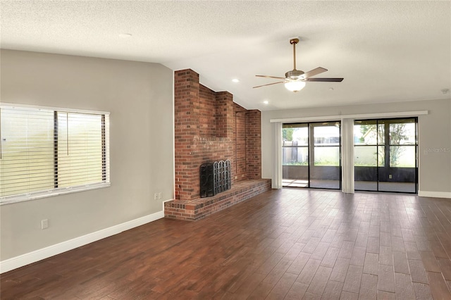 unfurnished living room with baseboards, lofted ceiling, dark wood-type flooring, a textured ceiling, and a brick fireplace