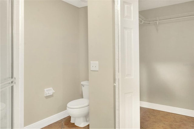 bathroom with tile patterned flooring, a walk in closet, baseboards, and toilet