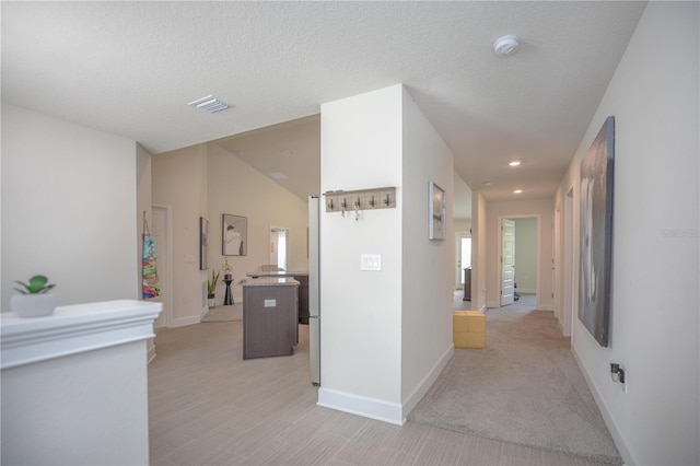 hall featuring vaulted ceiling, a textured ceiling, and light carpet