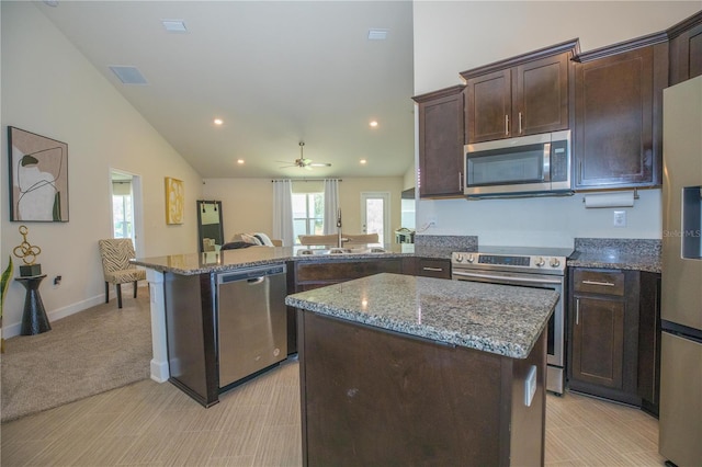 kitchen with light carpet, appliances with stainless steel finishes, dark stone counters, sink, and a kitchen island