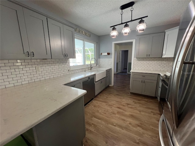 kitchen featuring gray cabinetry, pendant lighting, stainless steel appliances, sink, and light wood-type flooring