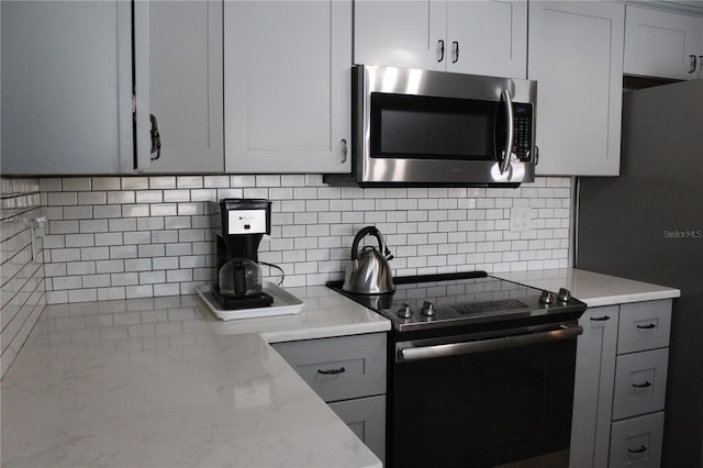 kitchen with backsplash, light stone counters, gray cabinets, and appliances with stainless steel finishes