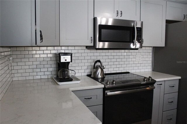 kitchen with black electric range oven, stainless steel microwave, tasteful backsplash, light stone countertops, and gray cabinetry