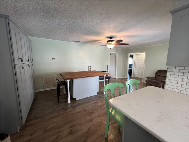 dining area with a ceiling fan, dark wood finished floors, visible vents, baseboards, and a textured ceiling