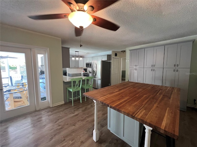 kitchen with appliances with stainless steel finishes, ceiling fan, dark wood-type flooring, a breakfast bar area, and pendant lighting