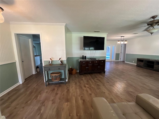 living room featuring a textured ceiling, ornamental molding, dark wood finished floors, wainscoting, and ceiling fan with notable chandelier