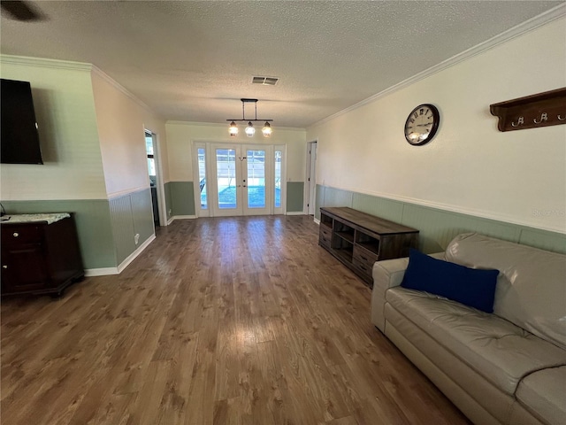 living area with wood finished floors, french doors, a wainscoted wall, crown molding, and visible vents