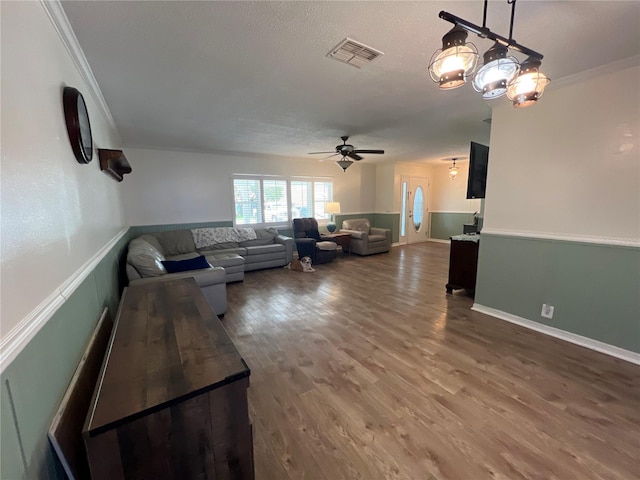 living room featuring a textured ceiling, crown molding, ceiling fan with notable chandelier, and wood-type flooring