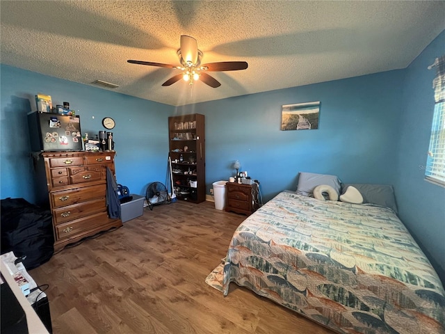 bedroom featuring ceiling fan, a textured ceiling, visible vents, and wood finished floors