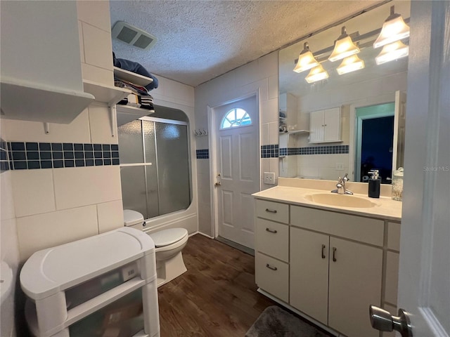 bathroom with toilet, enclosed tub / shower combo, wood finished floors, a textured ceiling, and vanity