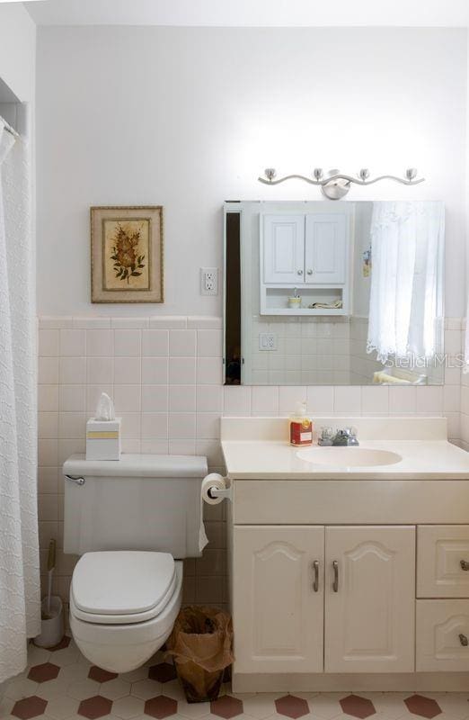 bathroom with tile walls, decorative backsplash, tile patterned floors, toilet, and vanity