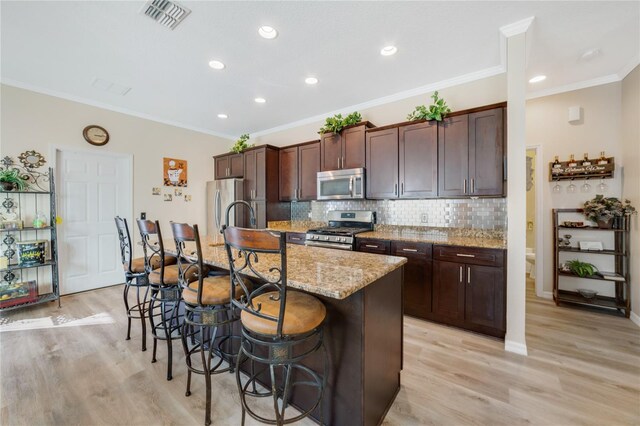 kitchen featuring a breakfast bar area, light stone counters, an island with sink, light hardwood / wood-style floors, and appliances with stainless steel finishes