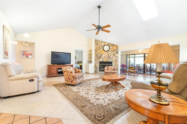 living area featuring light tile patterned floors, ceiling fan, a stone fireplace, high vaulted ceiling, and a skylight