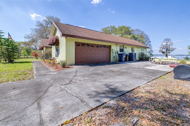 view of side of property with driveway, a garage, roof with shingles, cooling unit, and stucco siding