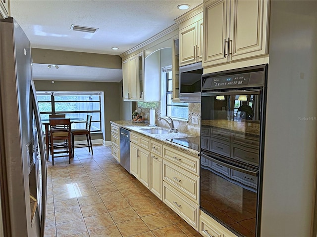 kitchen featuring light stone counters, cream cabinetry, black appliances, backsplash, and sink