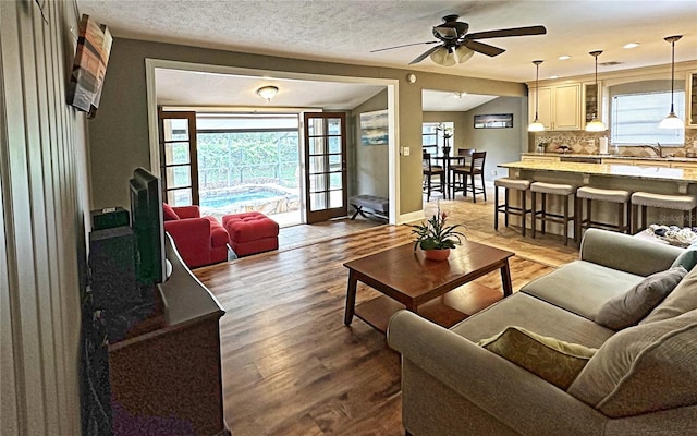 living room featuring ceiling fan, sink, a textured ceiling, and hardwood / wood-style flooring