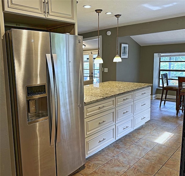 kitchen with pendant lighting, stainless steel refrigerator with ice dispenser, light stone counters, and light tile patterned floors