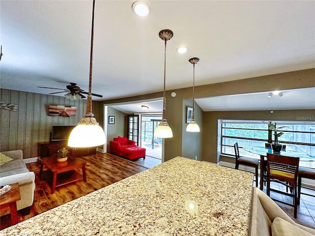 kitchen with hardwood / wood-style flooring, light stone counters, hanging light fixtures, and ceiling fan